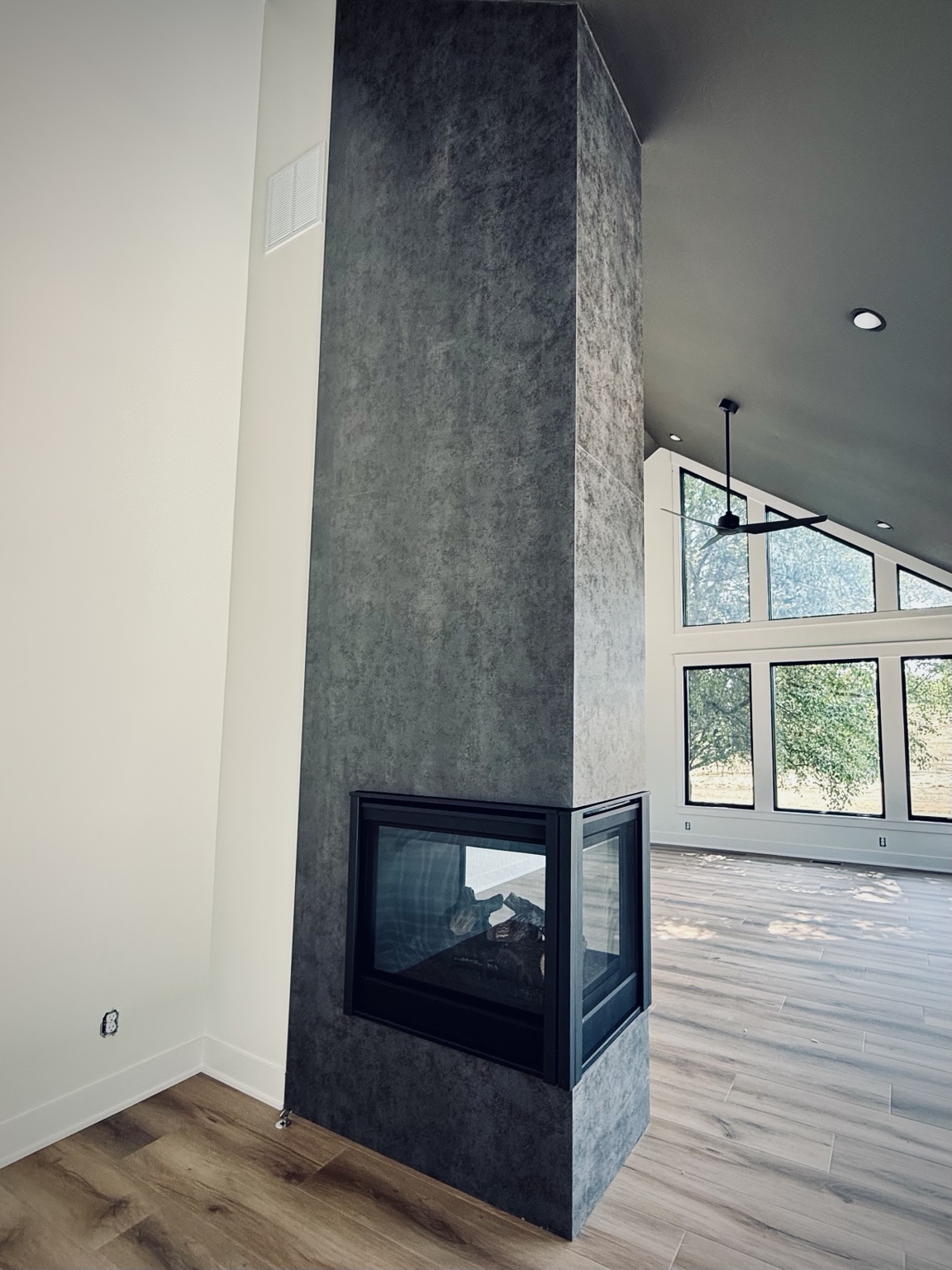 Tall dark stone fireplace framed by large windows